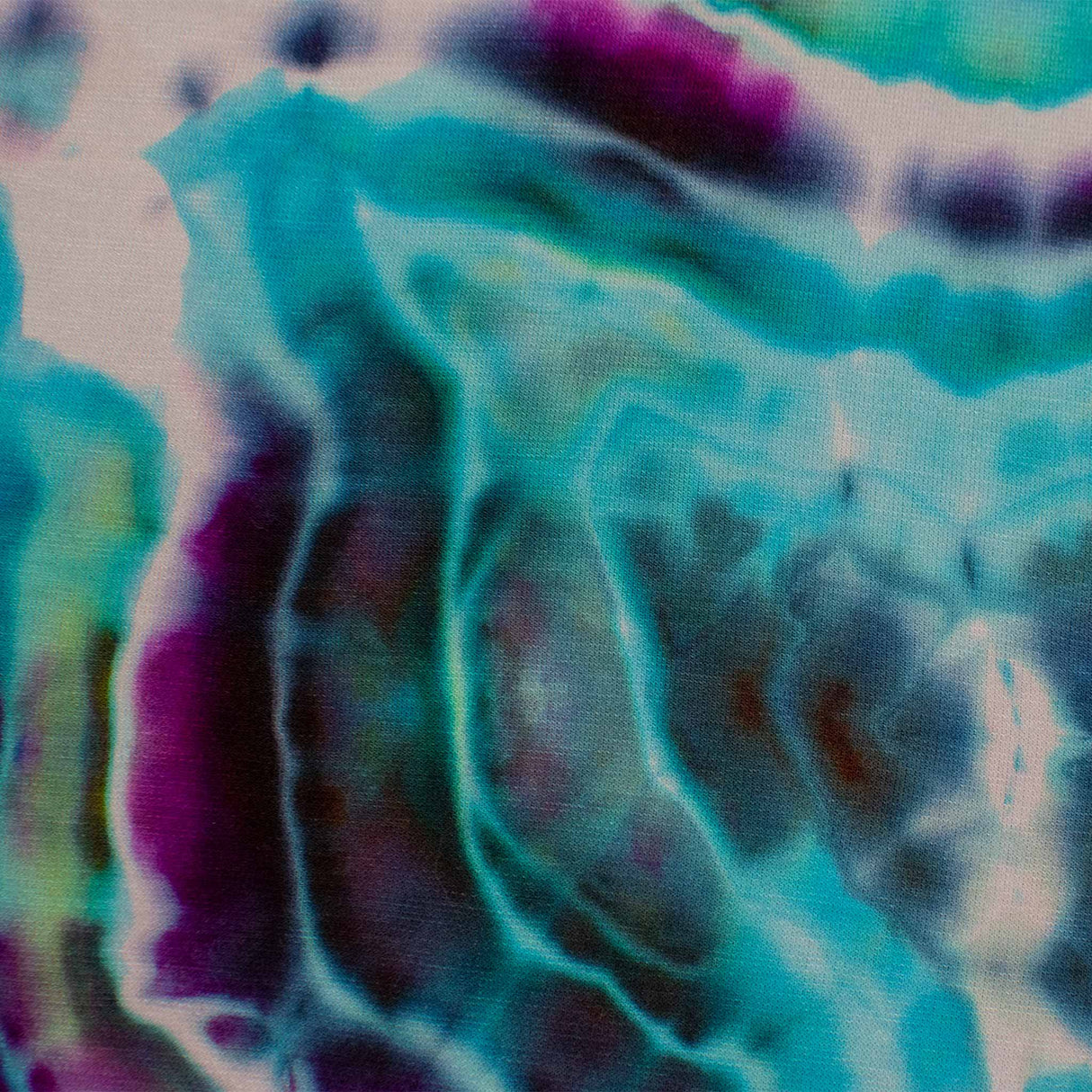 A pair of hand-dyed pants showcasing a unique ice-dye technique with organic patterns in a striking combination of sapphire, violet, and seafoam green.