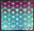 A 100% Cotton Bandana with a symmetrical tie-dye pattern in magenta, teal, aqua, and pale green, photographed flat against a dark background.